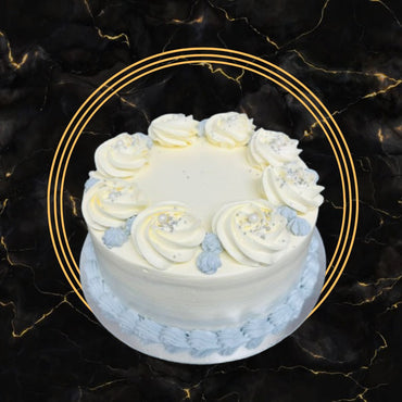 Elegant white and blue buttercream Fancy Cake decorated with swirls, edible pearls, and smooth frosting, freshly made by The Bakers Shop Birmingham.