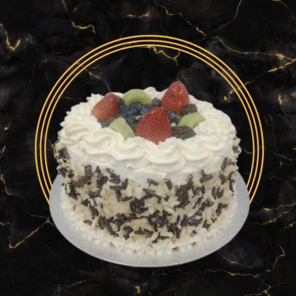 Vanilla cake topped with whipped cream, strawberries, blueberries, kiwi, and chocolate curls