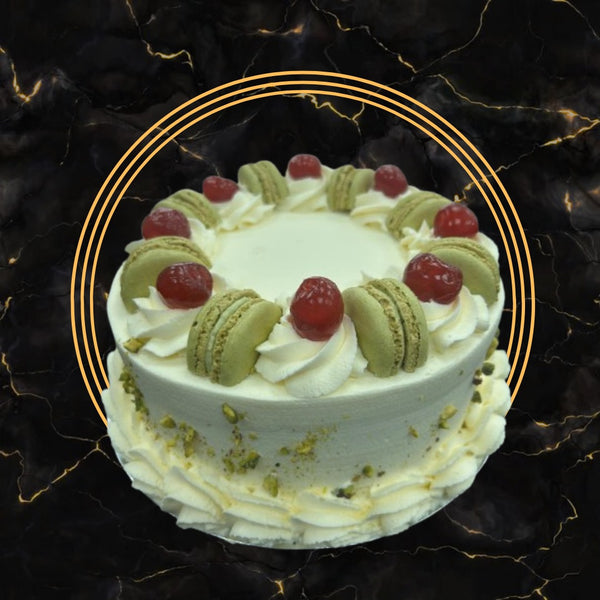 Elegant pistachio and cherry fancy cake topped with macarons, whipped cream swirls, and cherries, freshly made by The Bakers Shop Birmingham.
